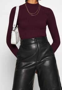 Haut à manches longues côtelé bordeaux associé à un short taille haute en cuir noir, présentant une texture brillante et un sac à main blanc embossé de crocodile.