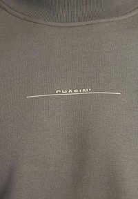 Gros plan sur un tissu gris avec un col côtelé et le texte blanc "QUASINI" au-dessus d'une fine ligne horizontale blanche centrée sur la poitrine.