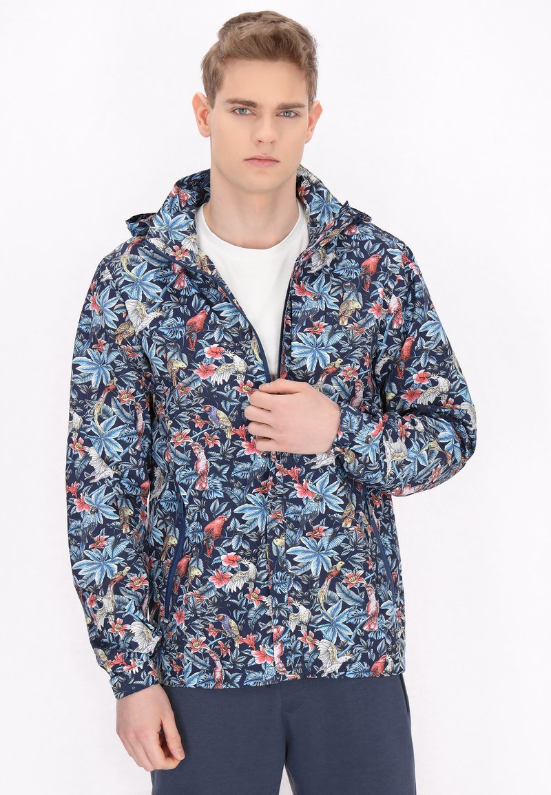 Giacca navy a fantasia floreale realizzata in materiale leggero, dotata di cappuccio, chiusura con zip e vivaci disegni di piante e uccelli rossi e blu.