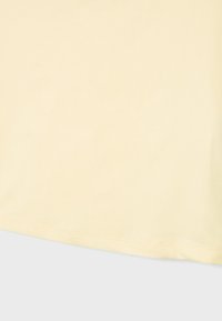 Tissu beige clair avec un ourlet légèrement arrondi et des coutures discrètes visibles le long du bord sur un fond gris clair.