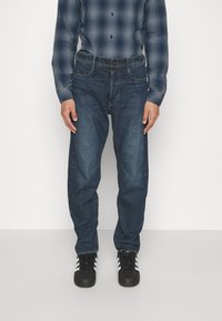 Mörkblå denimjeans med avslappnad passform, med en klassisk femficksdesign och subtila sömdetaljer. Bärs med en rutigt skorta.