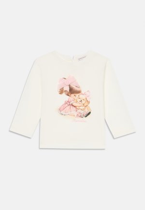 T-shirt branca de manga longa com uma ilustração pastel de uma rapariga com laços a acariciar um cão, com o texto "Mornalisa" abaixo.
