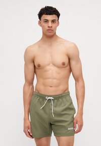 Shorts de bain verts en tissu léger, dotés d'une taille élastique, d'un cordon de serrage et d'un logo "BOSS" blanc sur le devant.
