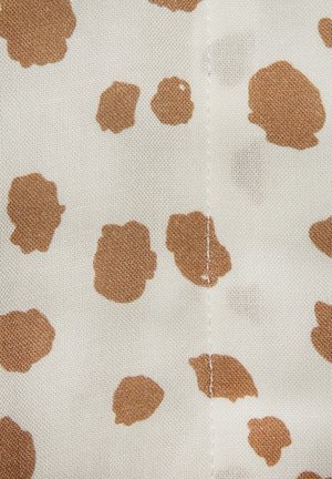 Hele kangaga, millel on beež taust ja ebaühtlased, abstraktsed pruunid laigud. Tekstuur on pehme ja keskel on nähtav õmbluse detail.