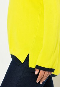 Maglione giallo lavorato a maglia con polsini e orlo a coste blu navy, dotato di spacchi laterali e una vestibilità comoda. Texture liscia e design leggero.
