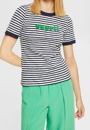 Kvinde iført en marineblå og hvid stribet kortærmet skjorte med grøn "esprit" tekst, kombineret med højtaljede klare grønne bukser.