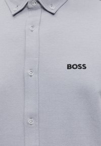 Chemise texturée gris clair à boutons avec col boutonné et « BOSS » brodé en noir sur la poitrine gauche.