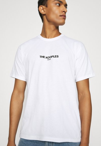 Tricou alb din bumbac cu mâneci scurte, având un logo negru "THE KOOPLES PARIS" centrat pe față. Textură netedă, croială lejeră.