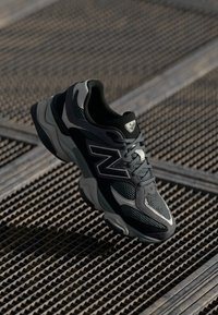 Baskets New Balance noires et grises en matériaux synthétiques et en maille, avec une semelle texturée et des accents réfléchissants. Design ajusté.