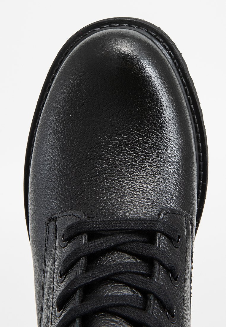 Scarpa in pelle nera con punta tonda, superficie texture e lacci neri. Presenta occhielli e cuciture lungo la suola.