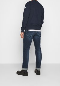 Marinblå sweatshirt med rund hals och långa ärmar, kombinerad med mörkblå denimjeans med uppvikta ärmslut och svarta ankelboots.