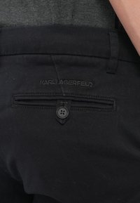 Čierne látkové nohavice so zadnou kapsou na gombík a jemným vyšitým logom. Hladká textúra a strih na mieru.