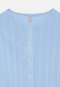 Ανοιχτό μπλε πλεκτό τοπ με κάθετες ρίγες και μικρές, διακοσμημένες τρύπες. Διαθέτει στρογγυλή λαιμόκοψη και λευκά κουμπιά κατά μήκος του μπροστινού μέρους.