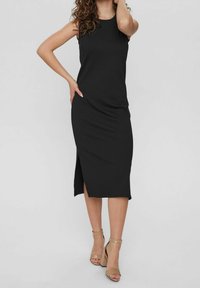 Robe midi noire à fines côtes sans manches avec fente sur le côté. Texture lisse et design ajusté, associée à des sandales à talons blocs beiges.