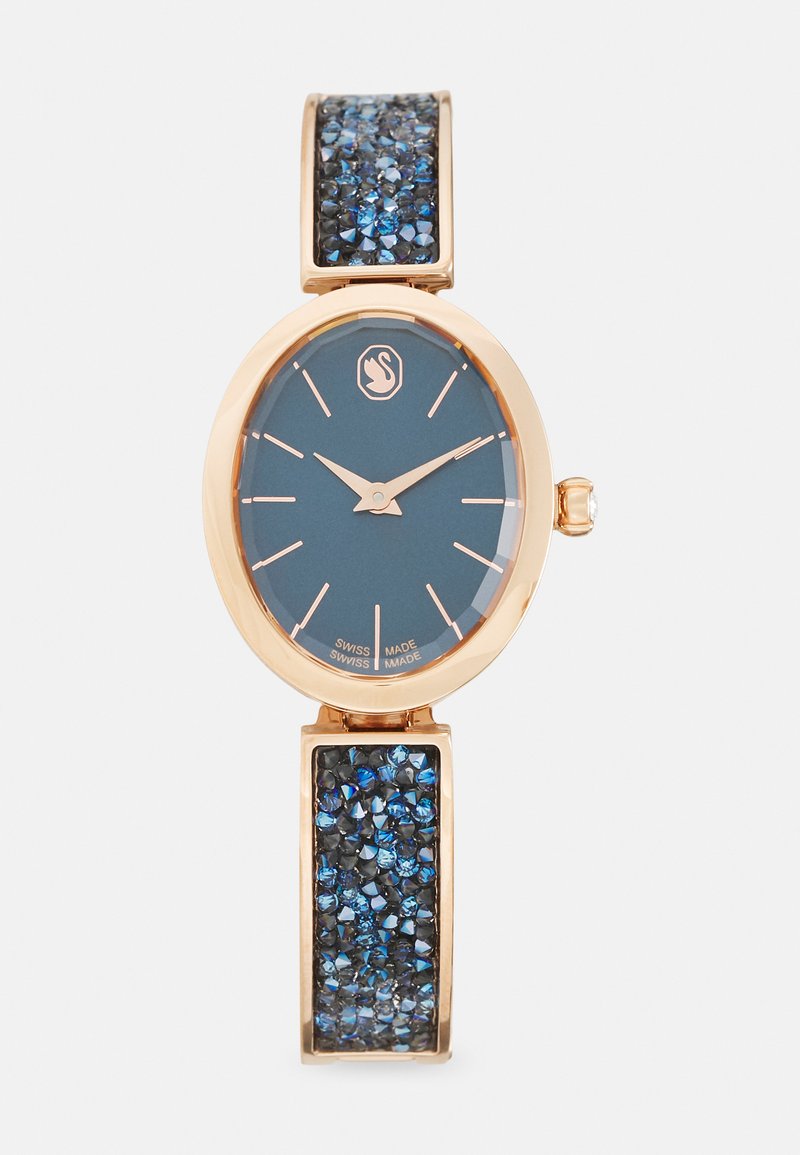 Reloj ovalado con una esfera azul oscura y acentos en oro rosa; presenta una correa adornada con embellishments de cristal azul para textura y detalle.