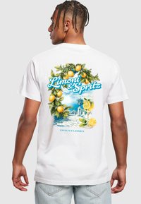 Camiseta de algodón blanca con un gráfico colorido de limones y una bebida, ambientada en una escena costera, con el texto "Limoni & Spritz."