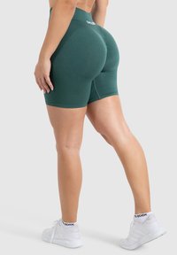Pantaloni sportivi verdi a vita alta realizzati in materiale elasticizzato, con una texture a costine e un logo del marchio visibile sull'elastico in vita.