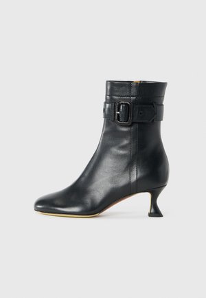 Black leather ankle boot with a pointed toe, tapered heel, and buckle detail at the cuff. Smooth texture and sleek design.