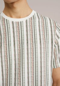 Rövidujjú pamut póló, zöld, piros és fehér függőleges csíkokkal. Ribbed kerek nyakkivágással és finom textúrázott mintával.