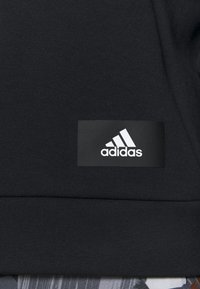 Tela de sudadera negra con una textura suave, que presenta una etiqueta rectangular negra con el logo blanco de "adidas" en la esquina inferior.
