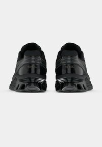 Par de sapatilhas atléticas pretas com amortecimento em gel, vistas de trás sobre um fundo branco simples.