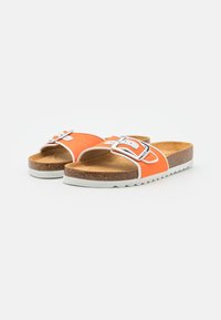 Sandales orange avec une boucle blanche, semelle en liège et matière supérieure texturée. Semelle extérieure en caoutchouc blanc avec un bord festonné.