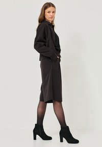 Casaco preto com um corte descontraído, combinado com uma saia preta até ao joelho e botas pretas de tornozelo com fecho e detalhe em corrente.