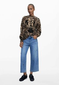 Svetr s leopardím vzorem a černou grafikou, doplněný světle modrými širokými džínami s vyšívanými detaily a černými teniskami.