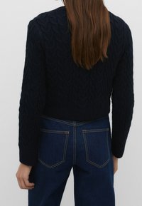 Marinblå stickad tröja med en strukturerad kabelmönster, kort design och ribbad nederkant. Matchad med hög midja, mörka denimjeans.