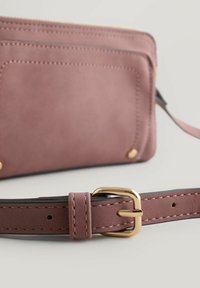 Cartera de ante rosa con múltiples detalles de costura y una correa con hebilla metálica dorada. Textura suave con detalles mínimos de herrajes.