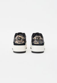 Black sneakers with a textured python print heel, white platform sole, and gold accent detailing, featuring a contrasting black suede upper.