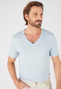 T-shirt azzurro chiaro a maniche corte con scollo a V, realizzato in tessuto morbido, presenta una vestibilità comoda e una trama liscia, abbinato a pantaloni color crema.