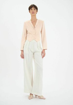 Blazer ajusté rose clair avec un col en V et trois boutons, associé à un pantalon large crème et des talons roses pâles avec des nœuds.