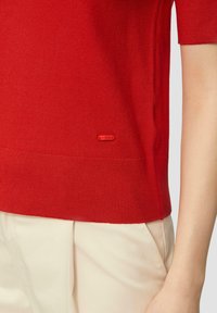 Top corto a maniche corte lavorato a maglia rossa con scollatura e orlo a costine, dotato di un piccolo etichetta logo rossa a contrasto sul lato della cucitura.