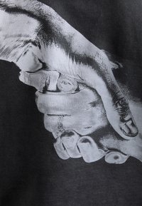 Textil negro con un gráfico de dos manos entrelazadas. Las manos están detalladas en blanco con textura de piel visible y sombras.