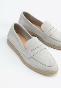 Šedé semišové loafers s hladkým povrchem, mají prošívaný horní pásek a světlou hnědou gumovou podrážku. Minimalistický design.