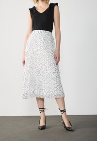 Top sin mangas negro con hombros con volantes, combinado con una falda blanca plisada con lunares negros. Tacones negros de punta.