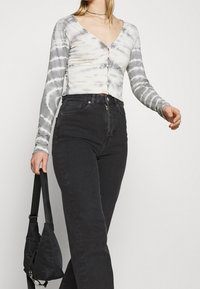 Top corto de manga larga en tie-dye gris y blanco con escote en V y cierre de botones, combinado con jeans negros de cintura alta y un bolso negro.