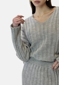 Ljust grått stickat set bestående av tröja och matchande kjol med vertikalt ribbad textur, med V-ringning och vida ärmar.
