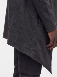 Dark gray asymmetrical long sleeve top with side pocket worn over black pants, showing a person's arm and hand at the side.