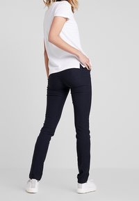 Vit kortärmad topp som matchas med mörkblå slim-fit byxor och vita sneakers. Materialet verkar slätt, med en enkel design.