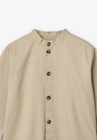 Camicia button-up khaki con colletto alla mandarina, sette bottoni marroni, texture a coste e maniche lunghe. Design semplice, senza motivi o dettagli.