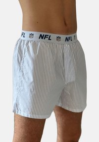 Mann trägt weiße Boxershorts mit dünnen blauen vertikalen Streifen und einem weißen Bund mit NFL-Logos und -Schriftzug.