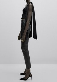 Black satin crop top with spaghetti straps, paired with slim black leather pants and black pointed-toe heels, featuring a tied detail at the shoulder.