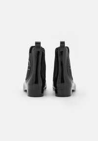 Botas de tobillo de charol negro con paneles laterales elásticos, lengüetas y un acabado suave. Presenta un bajo tacón cuadrado y una sutil marca.