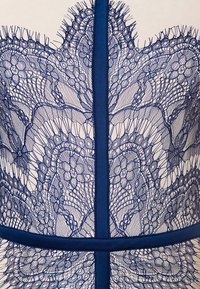 Námořnická modrá krajková šaty s složitými květinovými vzory, síťovinovými detaily a pevným modrým akcentem kolem výstřihu a pasu.