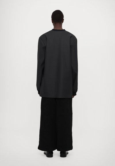 Chemise noir oversize à manches longues avec un col rond, associée à un pantalon noir texturé à jambes larges, vue de dos.