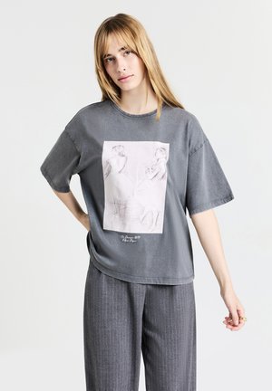 T-shirt oversized grigio in cotone, con una stampa frontale di due ballerini in uno stile di schizzo leggero. Texture morbida e vestibilità rilassata.