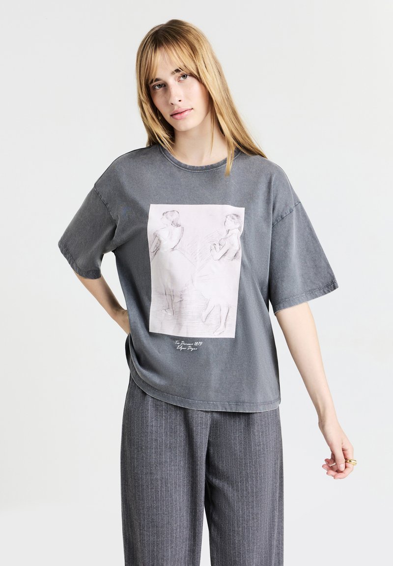 T-shirt oversize gris en coton, avec un imprimé à l'avant représentant deux danseurs dans un style de croquis léger. Texture douce et coupe décontractée.