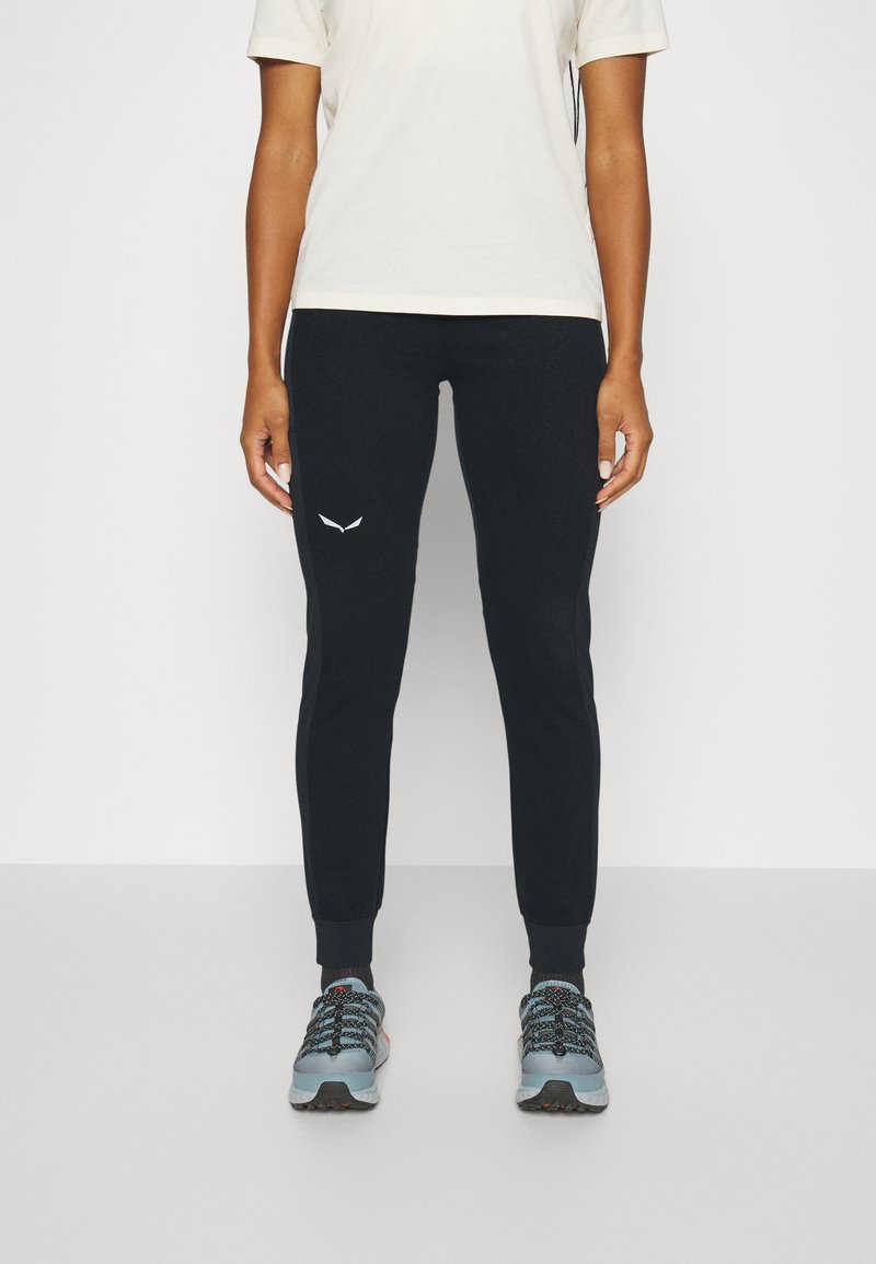 Mørk marineblå joggebukser med logo i hvitt, laget av mykt stoff. Kombinert med grå treningssko med svarte og røde detaljer.